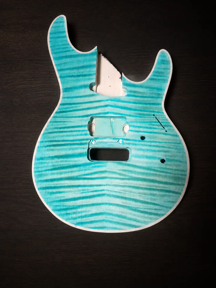 Aqua figured-maple guitar body in progress on a professional studio background