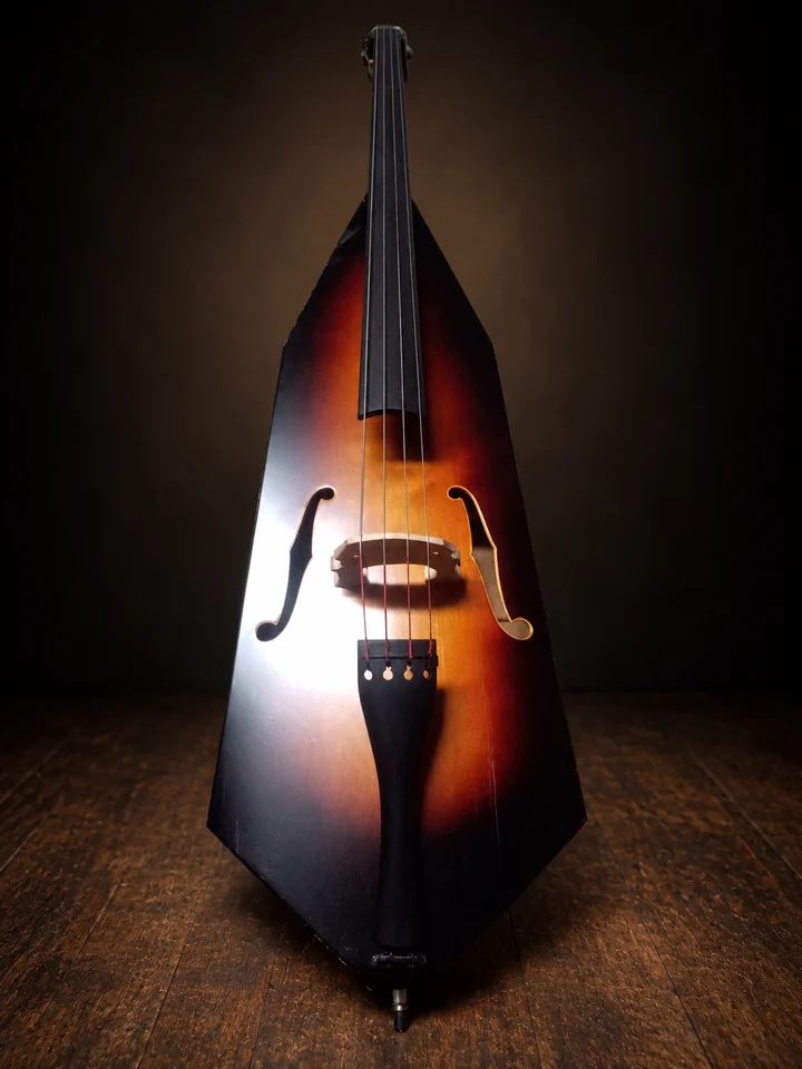 Sunburst upright instrument with four strings, a carved bridge and black tailpiece on a dark studio background